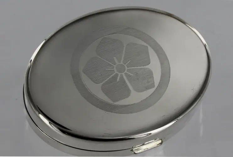 A silver compact with a flower on it.