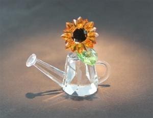 A glass watering can with a sunflower in it.